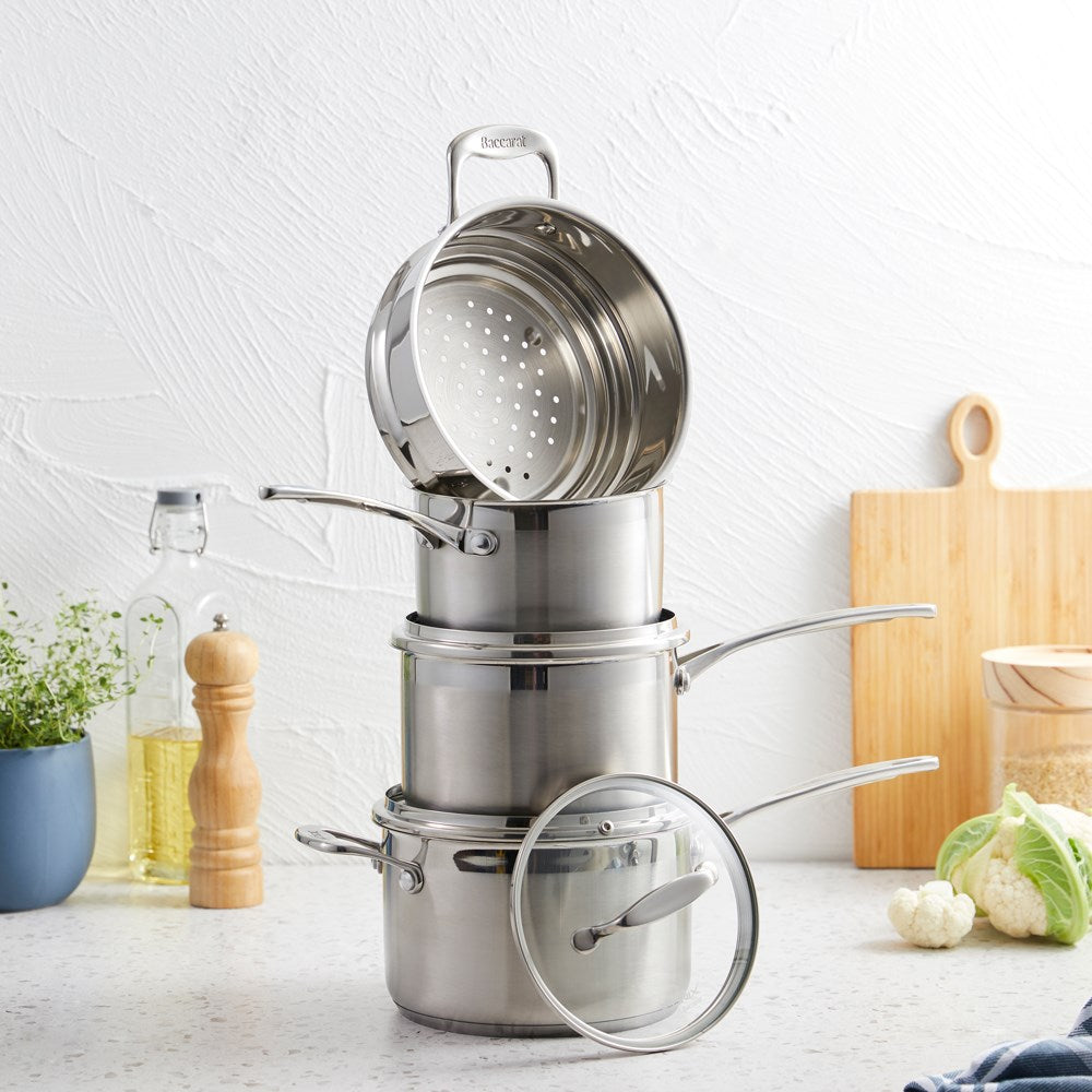 A set of polished stainless steel cookware with fresh vegetables on a wooden board - Baccarat Iconix