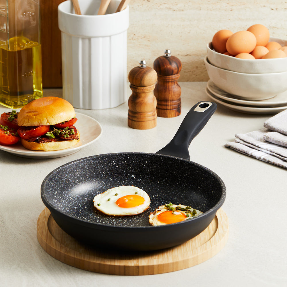 Person cooking vegetables in a granite frying pan 28cm with a pepper grinder nearby - Baccarat