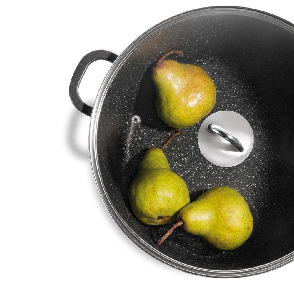 Top-down view of a black speckled pot or pan containing three green pears, with a silver metal handle visible on the lid, set against a plain white background.
