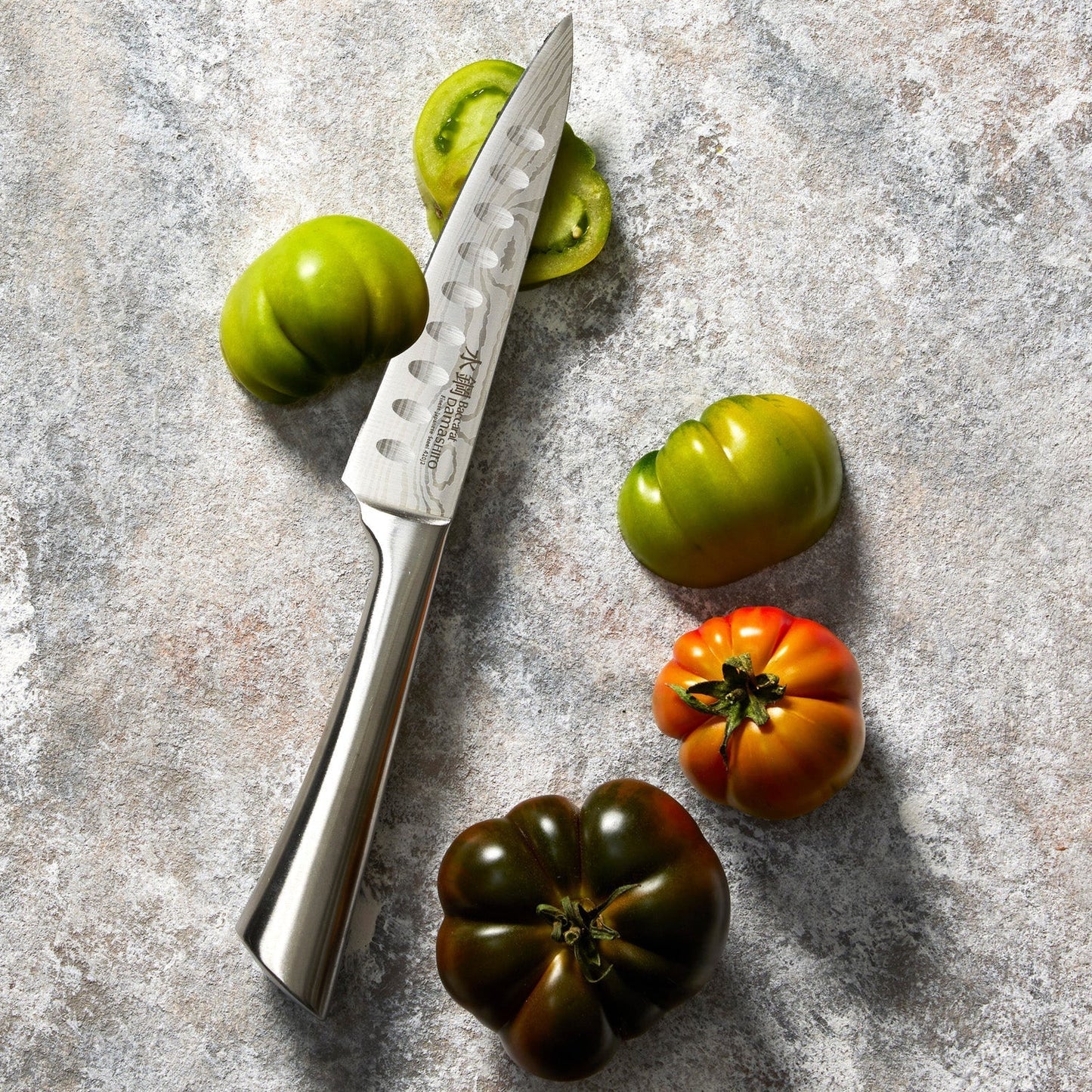 Fresh heirloom tomatoes on a grey surface with green and orange produce - Baccarat damashiro