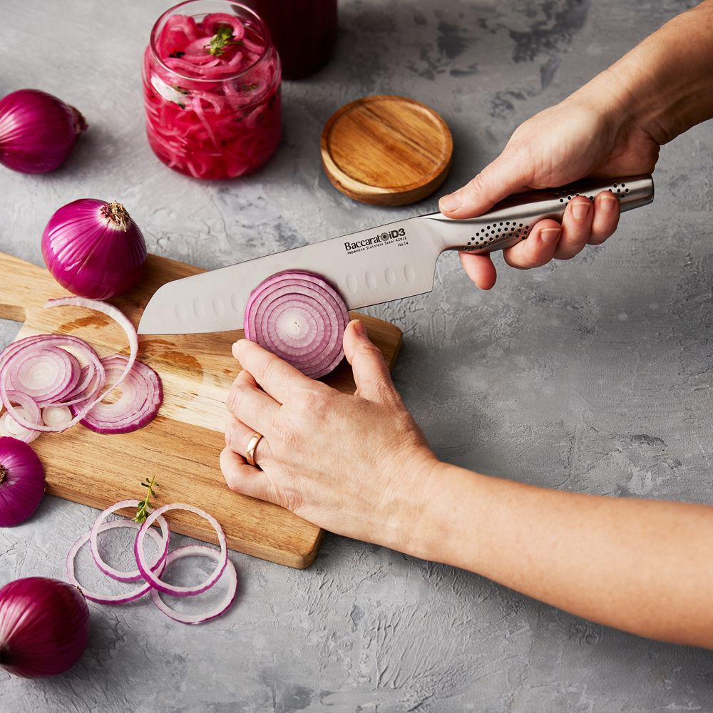 A person slices a red onion on a wooden board with a sharp knife - Baccarat id3 santoku knife 18cm