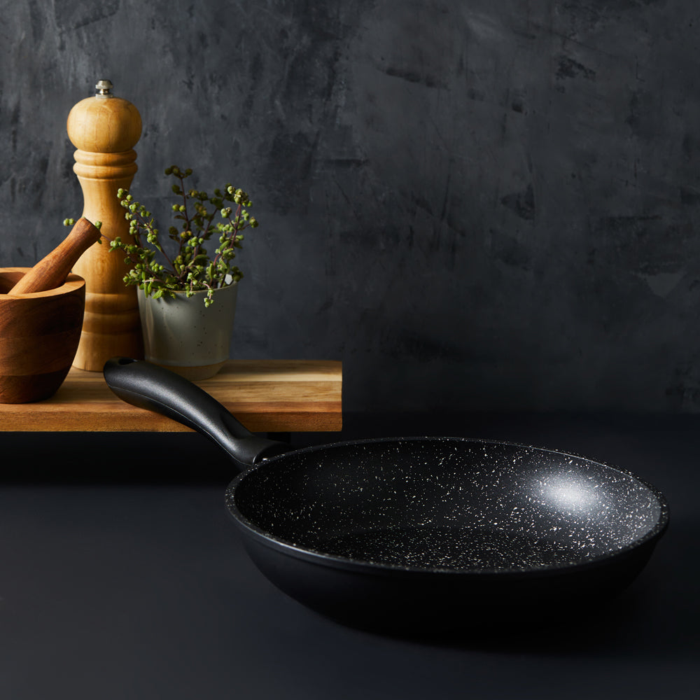 A hand holds a frying pan with grilled salmon and lemon slices stone grey - Baccarat