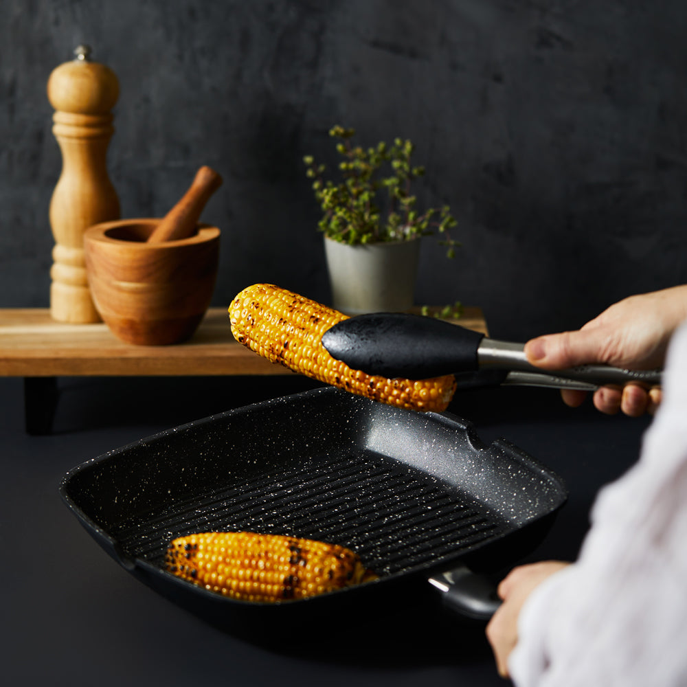 Person grilling corn with a black stone grill pan and spices nearby - Baccarat