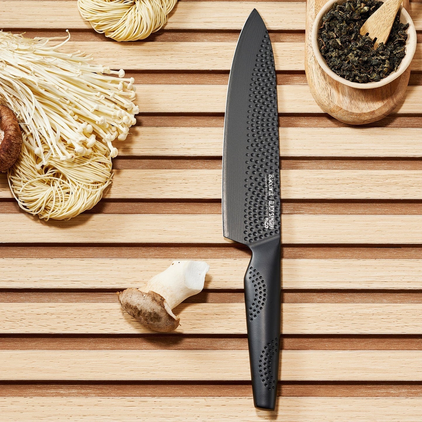 Sharp Black Samurai chef's knife on wooden surface with dried herbs and mushrooms - Baccarat ID3