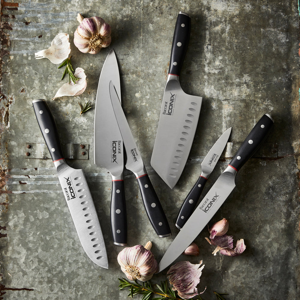 A sleek santoku knife with black handle on a wooden strip against a grey wall knife - Baccarat