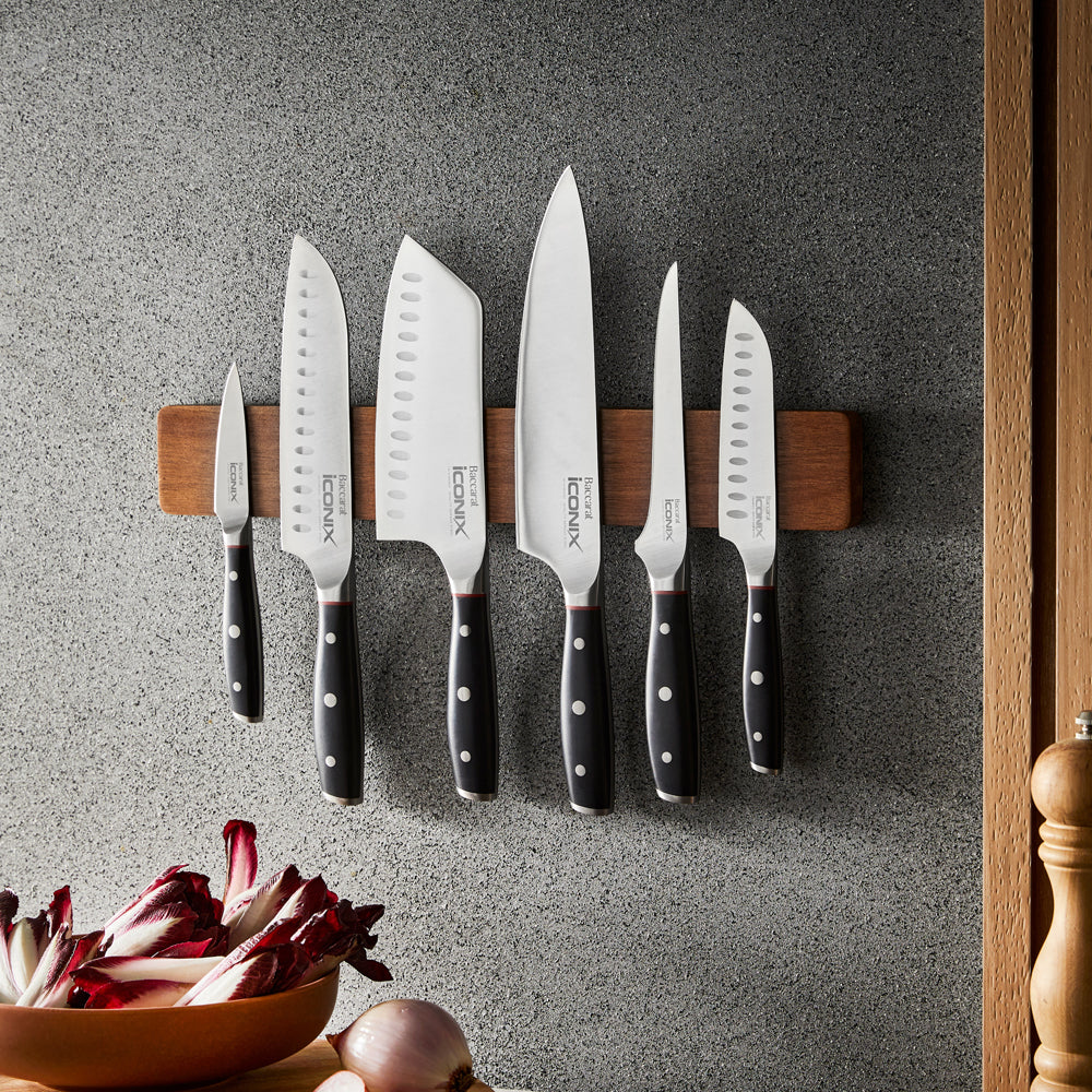 A sleek santoku knife with black handle on a wooden strip against a grey wall knife - Baccarat