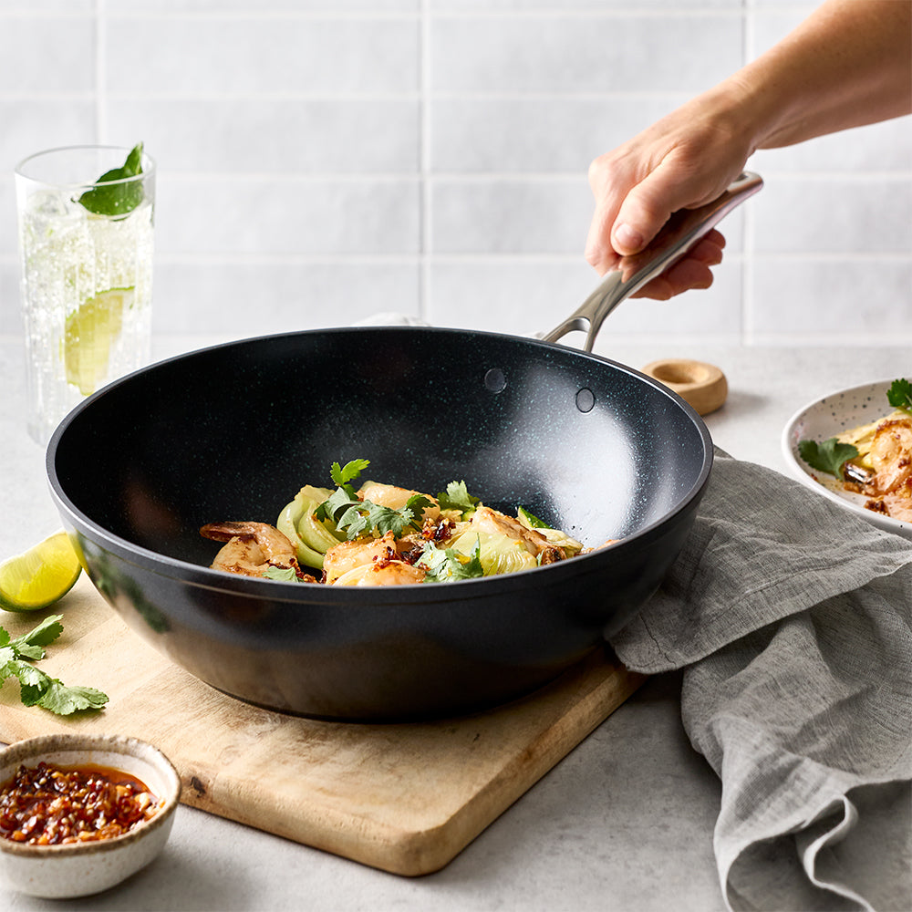 A person is holding the handle of the black frying pan filled with cooked food on a counter.