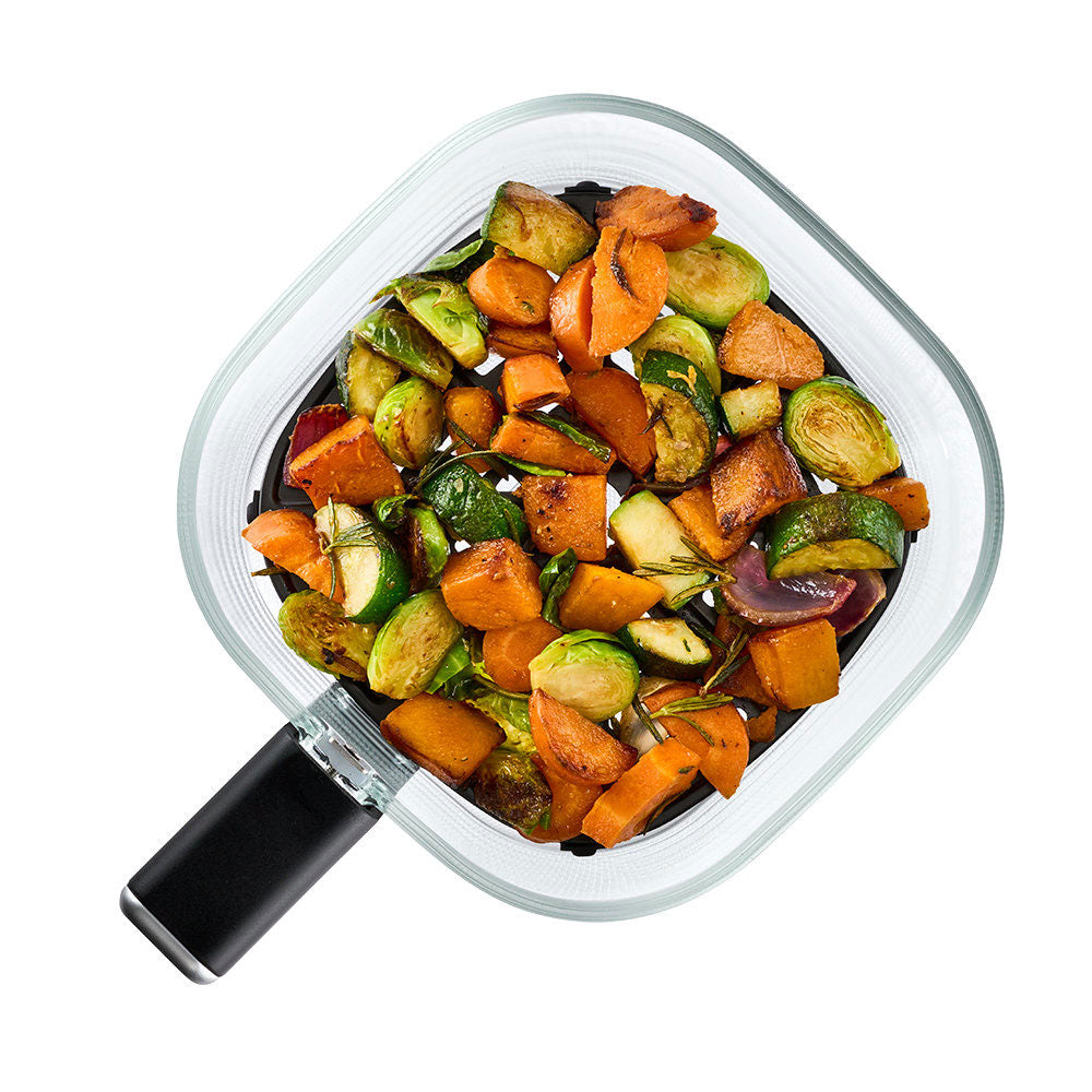 Overhead view of a square glass baking pan with a black handle, filled with roasted vegetables including sweet potatoes, Brussels sprouts, and onions, on a white background.