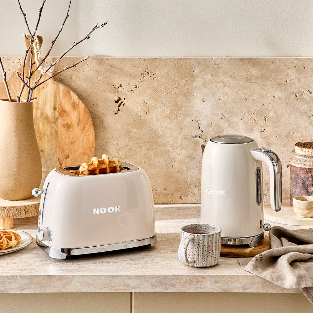 Cream-colored Nook brand toaster and electric kettle set on a beige stone countertop in a styled kitchen setting.