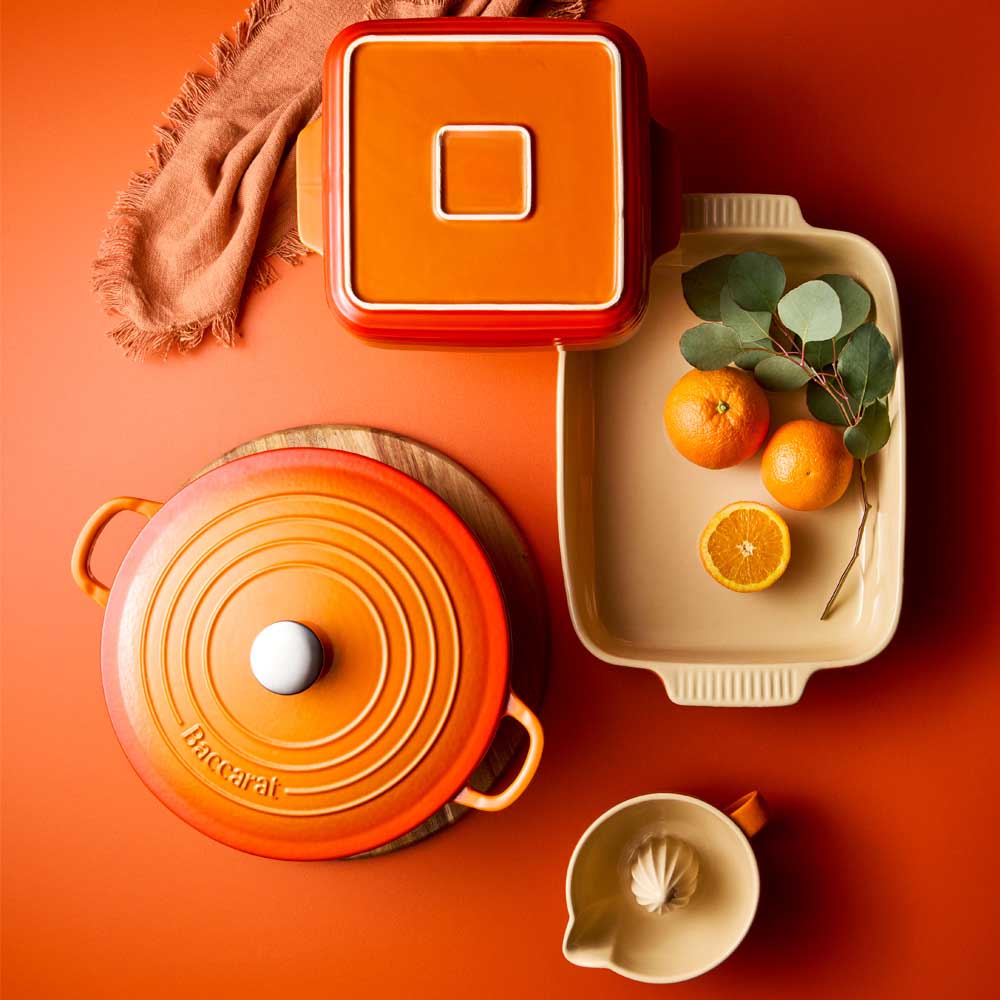 A flat-lay layout of orange kitchen accessories is arranged on a surface.
