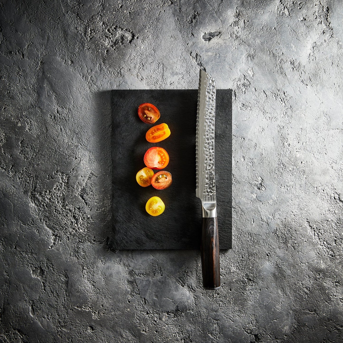 A Baccarat Emperor 20cm bread knife with a sharp edge on a wooden surface surrounded by other knives