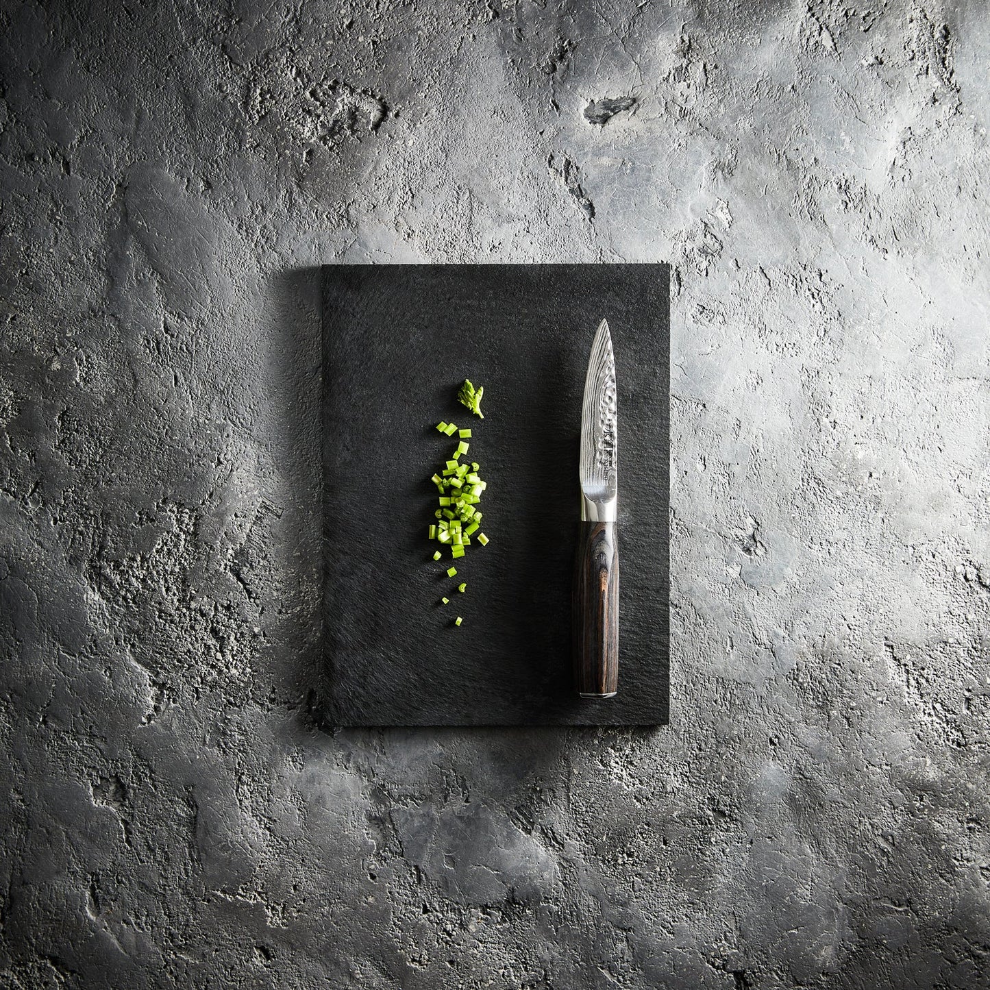 Chopped green herbs on a dark cutting board with a sleek silver knife - Baccarat Damashiro Emperor