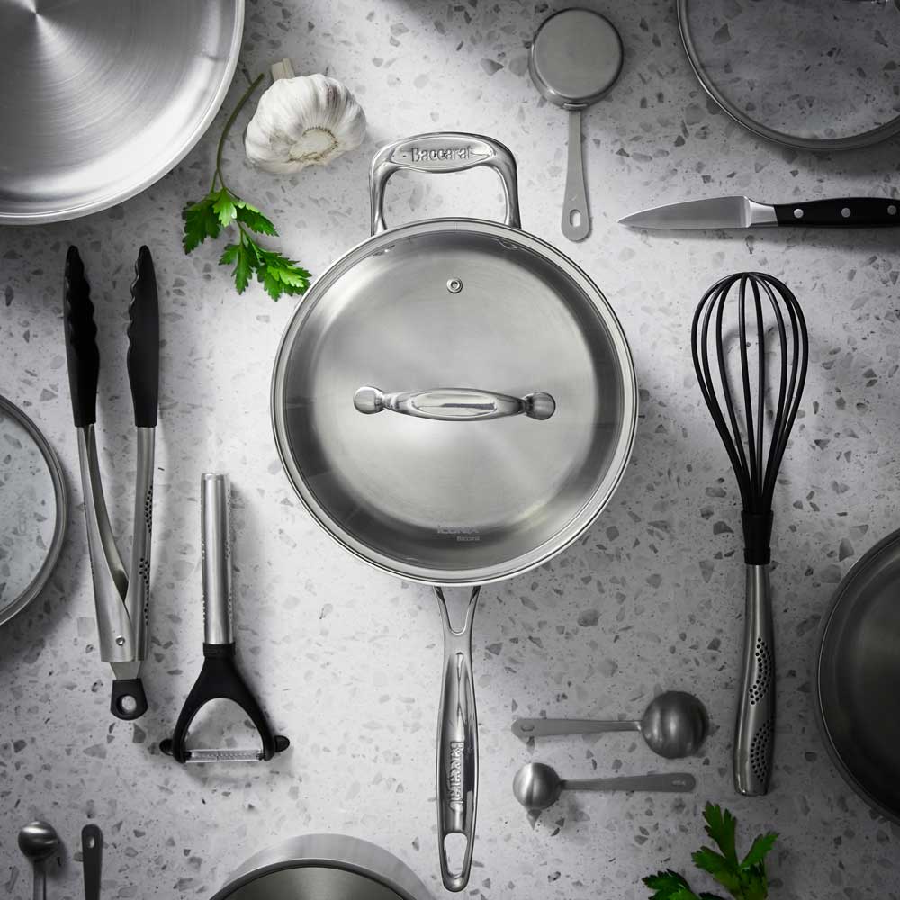 Pasta being poured into a saucepan on a wooden surface with an olive oil bottle - Baccarat