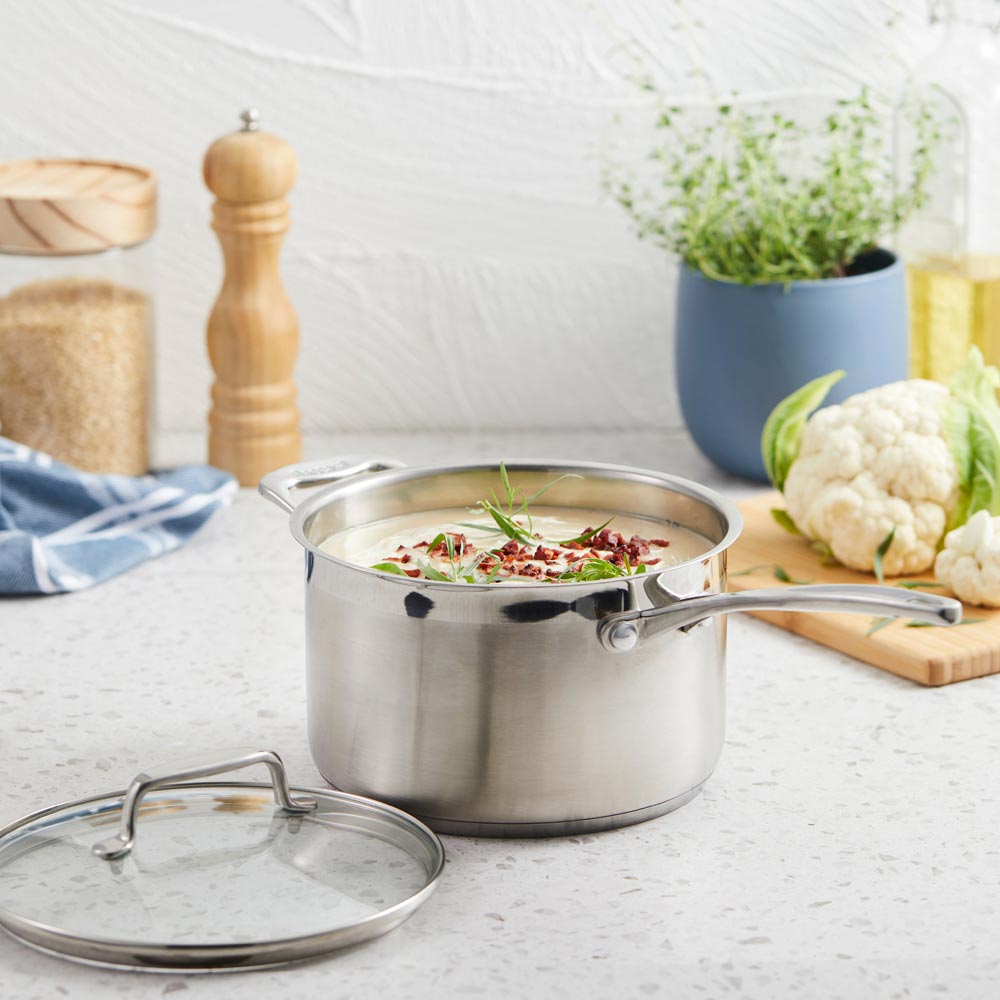 A set of polished stainless steel cookware with fresh vegetables on a wooden board - Baccarat Iconix