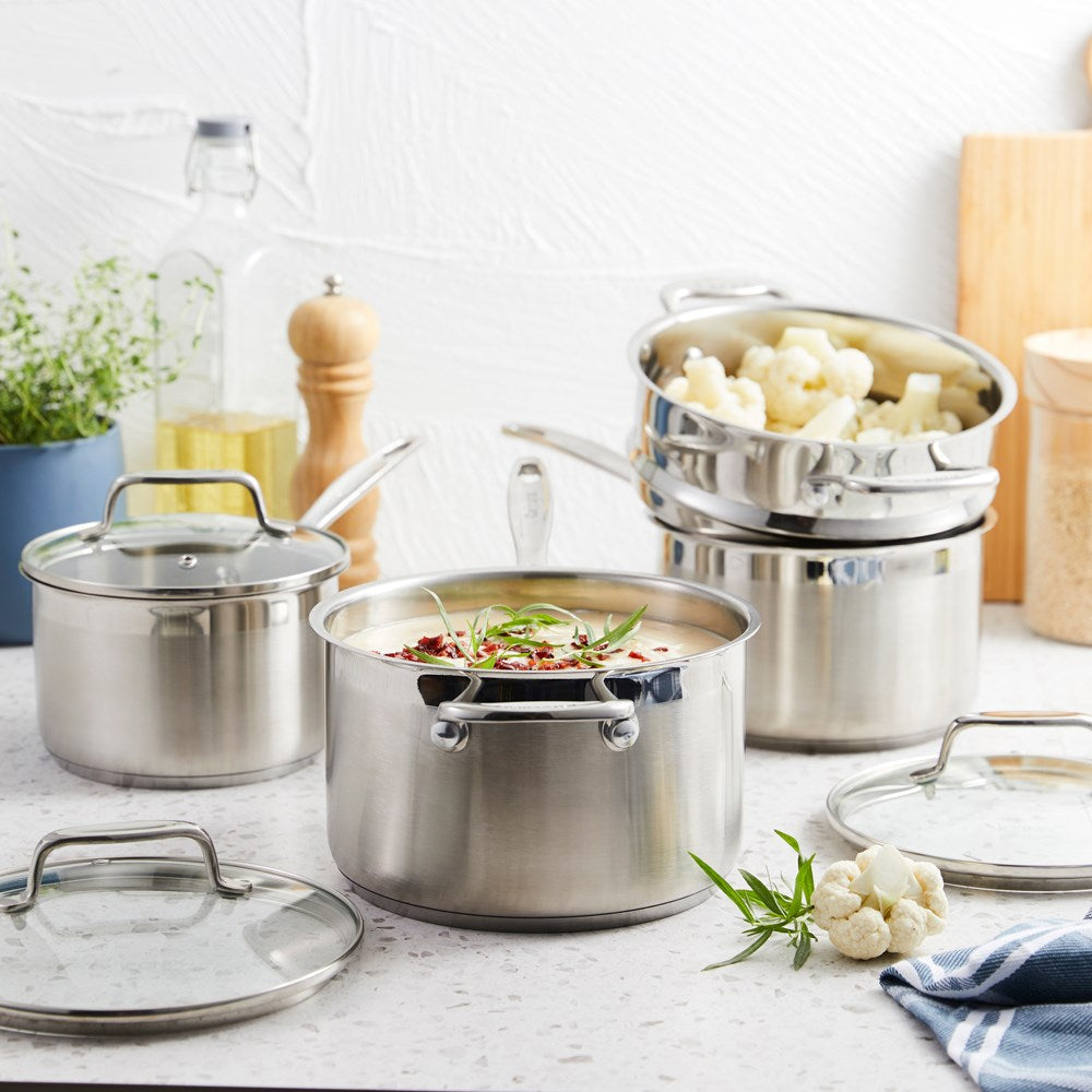 A set of polished stainless steel cookware with fresh vegetables on a wooden board - Baccarat Iconix