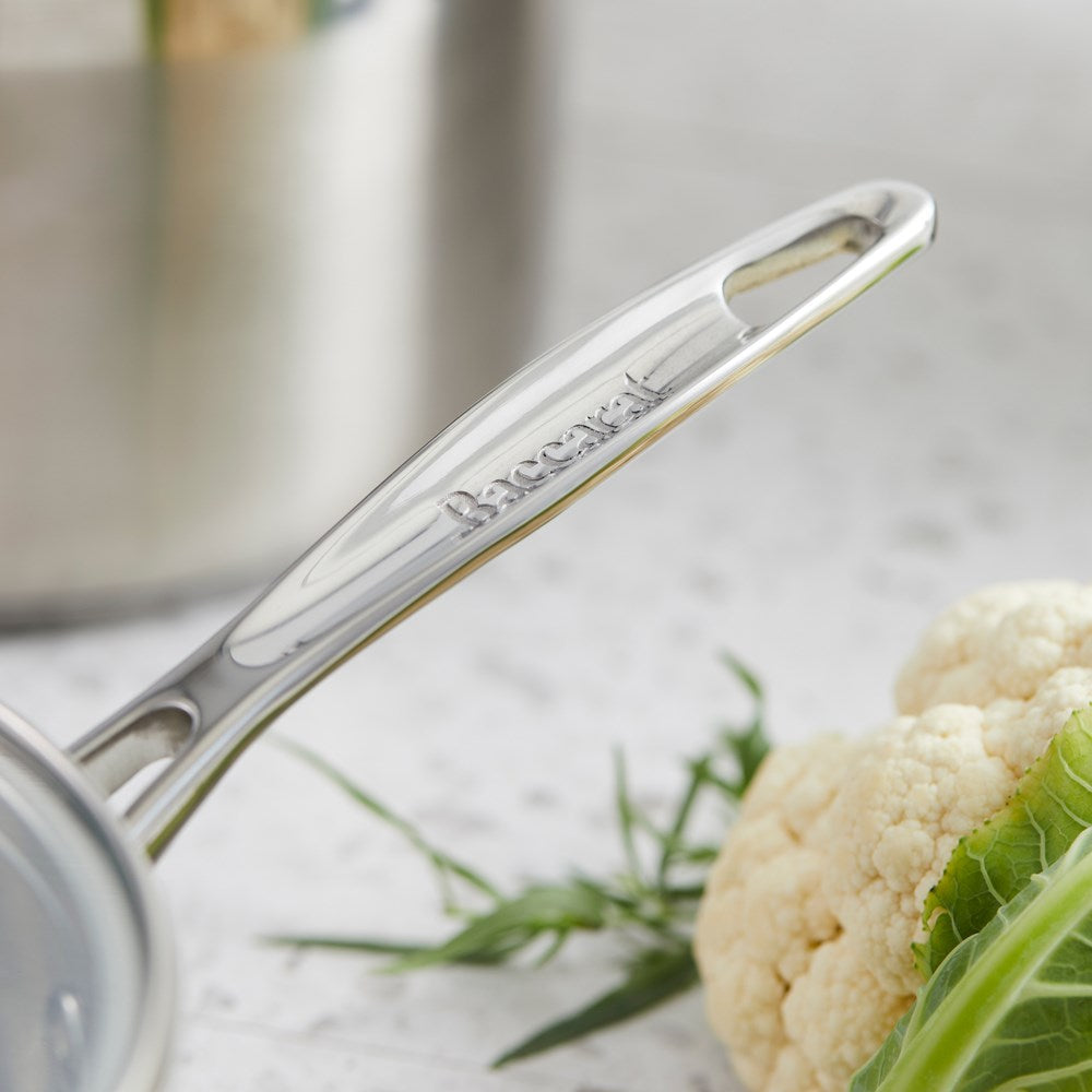 A set of polished stainless steel cookware with fresh vegetables on a wooden board - Baccarat Iconix