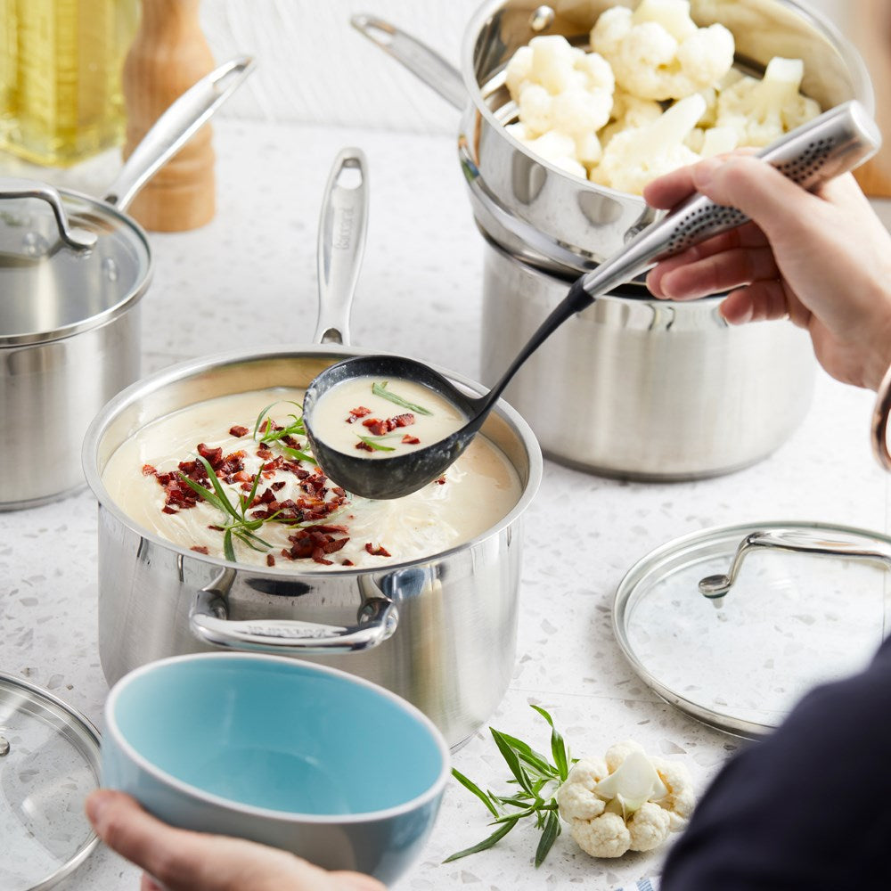 A set of polished stainless steel cookware with fresh vegetables on a wooden board - Baccarat Iconix