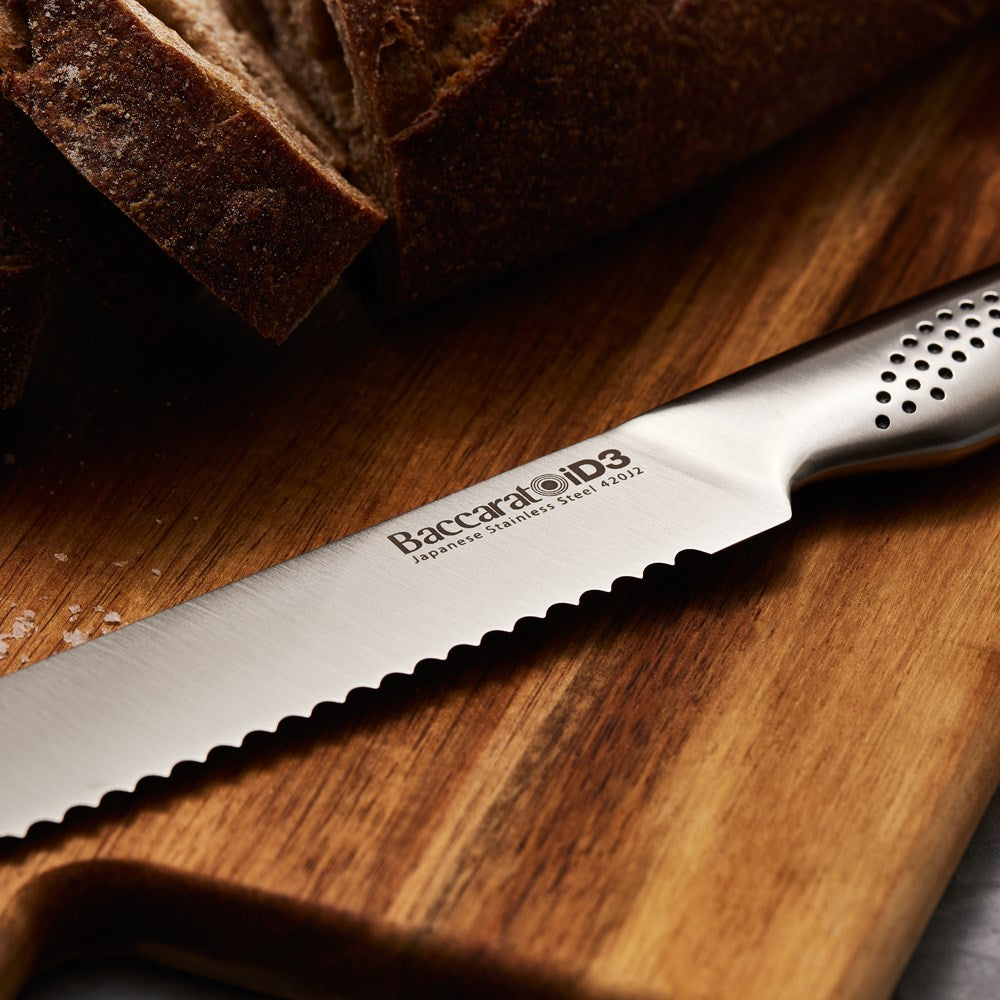 A sleek serrated bread knife is positioned on a wooden cutting board next to fresh bread - Baccarat