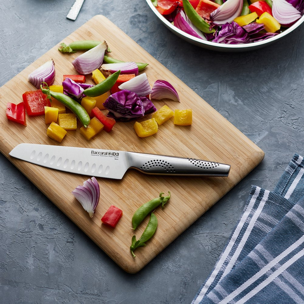 A sleek santoku knife rests on a wooden board surrounded by colourful sliced vegetables - Baccarat