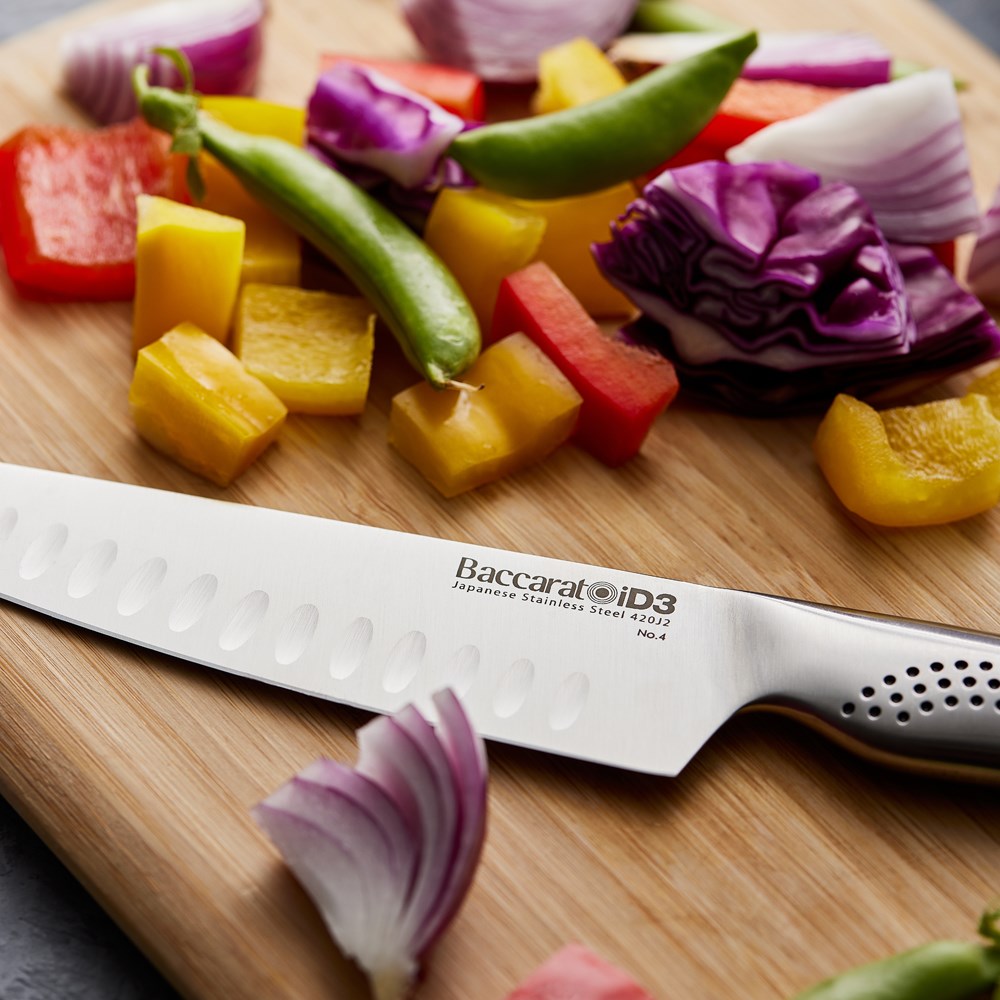 A sleek santoku knife rests on a wooden board surrounded by colourful sliced vegetables - Baccarat