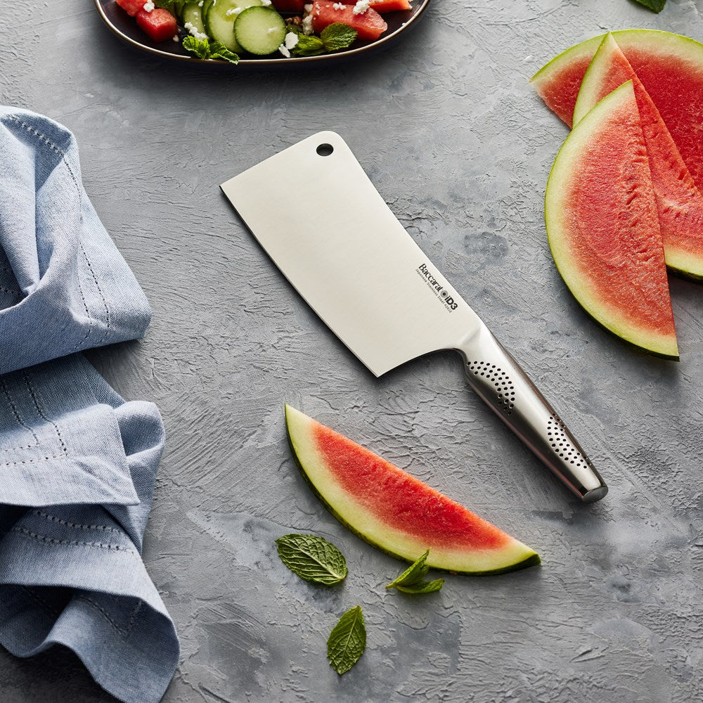 Person slicing watermelon with a cleaver next to a salad on a gray countertop - Baccarat