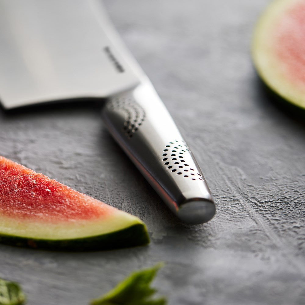 Person slicing watermelon with a cleaver next to a salad on a gray countertop - Baccarat