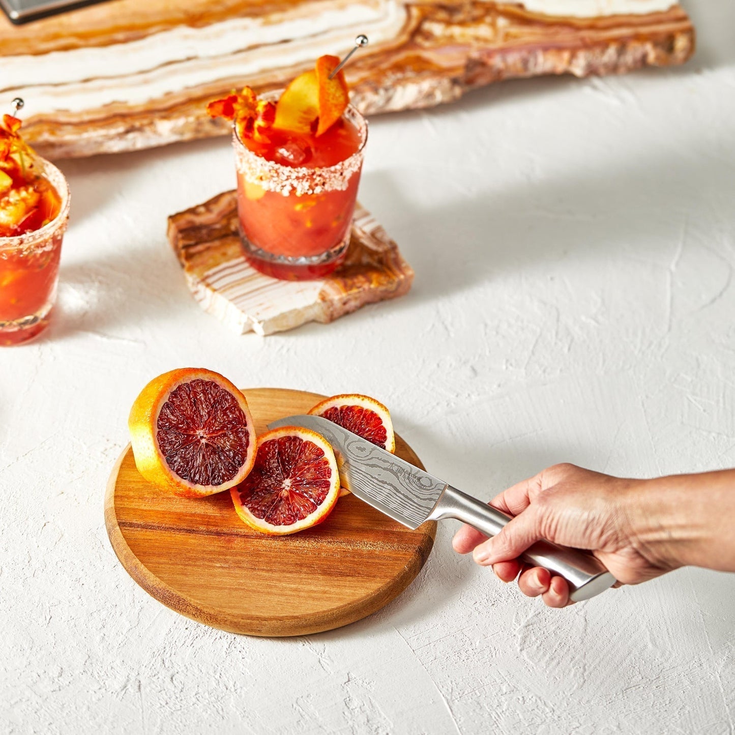 Sliced blood oranges on a wooden board with a knife in hand vibrant orange hues - Baccarat Damashiro