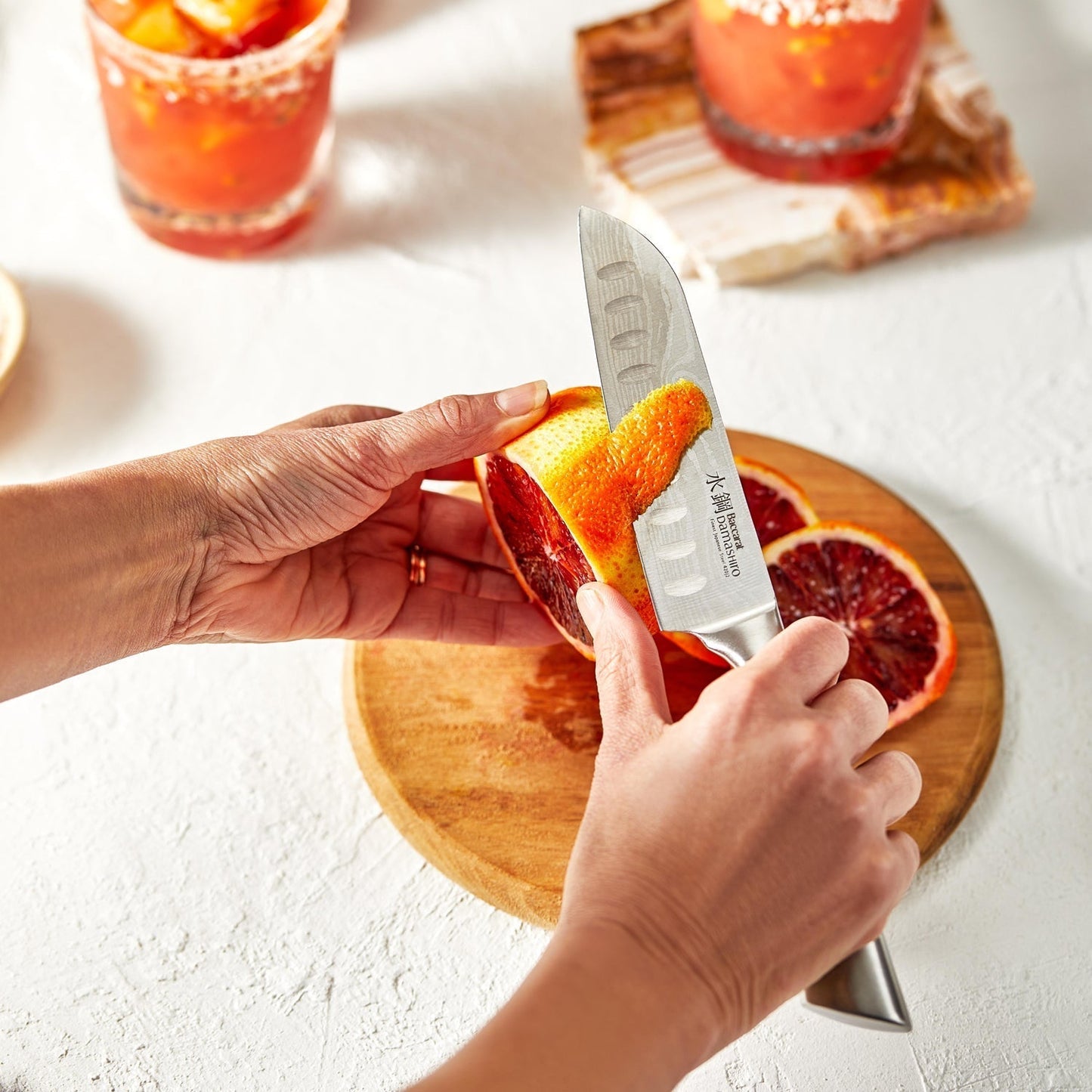 Sliced blood oranges on a wooden board with a knife in hand vibrant orange hues - Baccarat Damashiro
