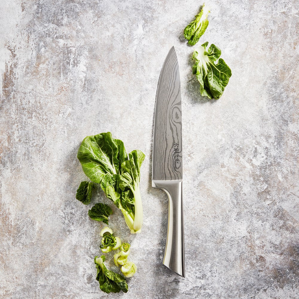 A person chopping green vegetables with a silver knife on a marble countertop - Baccarat damashiro
