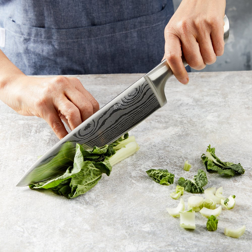 A person chopping green vegetables with a silver knife on a marble countertop - Baccarat damashiro