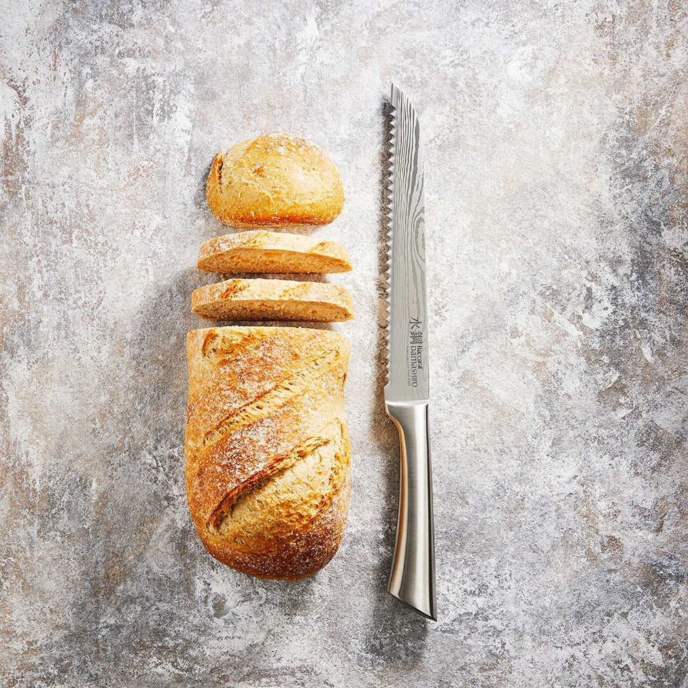 Golden brown bread slices beside a Baccarat Damashiro Bread Knife 20cm on a textured surface