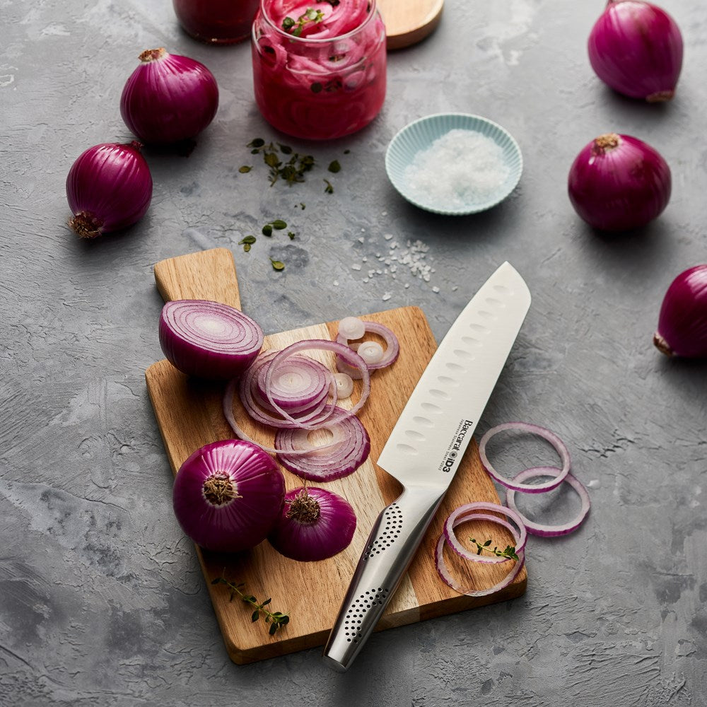 A person slices a red onion on a wooden board with a sharp knife - Baccarat id3 santoku knife 18cm