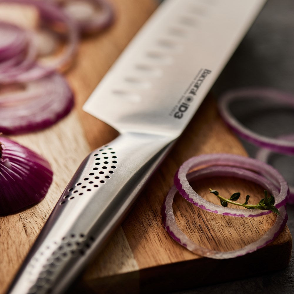 A person slices a red onion on a wooden board with a sharp knife - Baccarat id3 santoku knife 18cm
