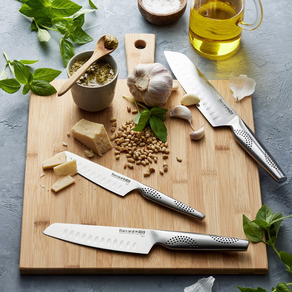 Three santoku knives resting on a wooden cutting board with fresh herbs and vegetables - Baccarat