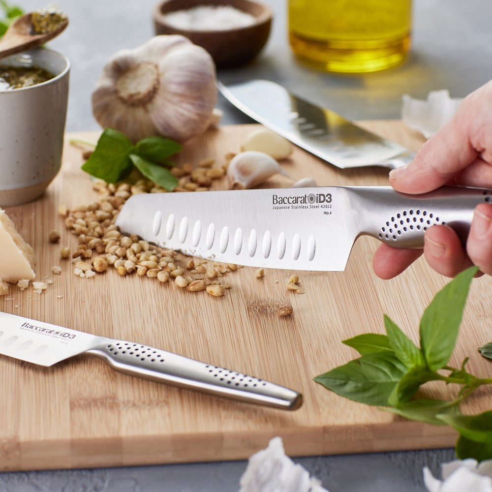 Three santoku knives resting on a wooden cutting board with fresh herbs and vegetables - Baccarat