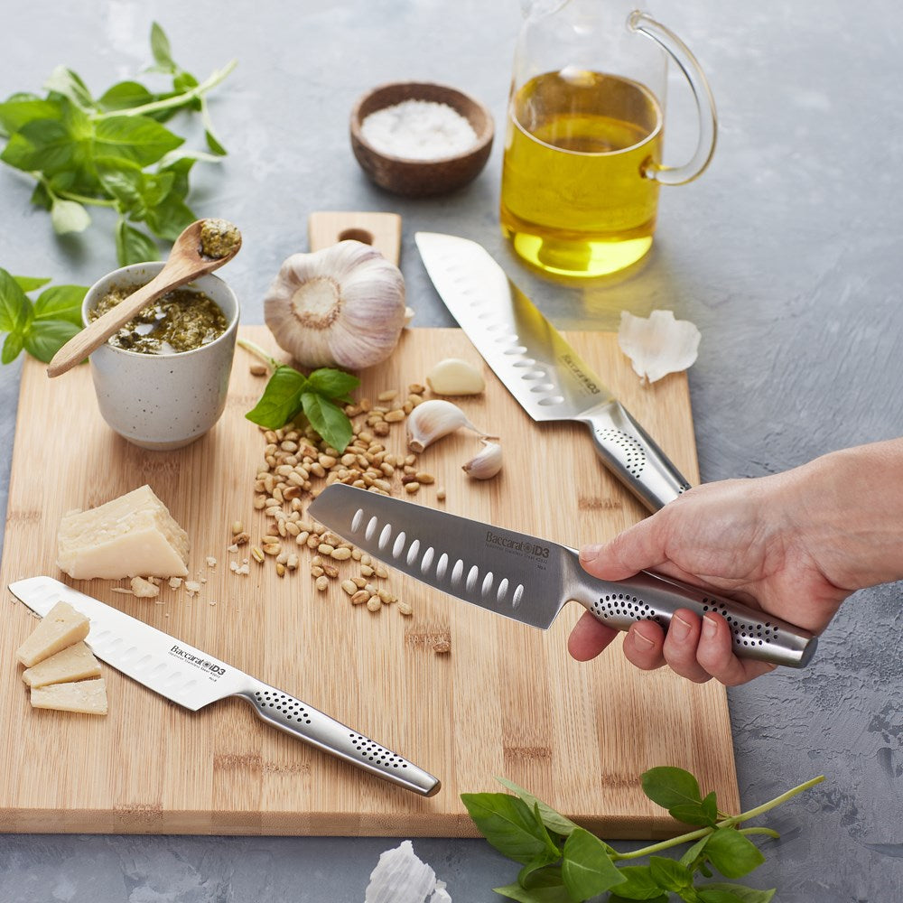 Three santoku knives resting on a wooden cutting board with fresh herbs and vegetables - Baccarat