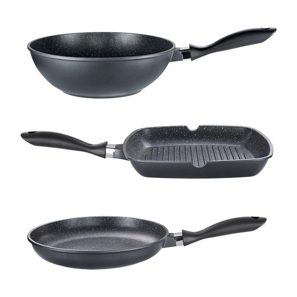 Three frying pans and a grill pan on a dark counter with wooden utensils and herbs - Baccarat
