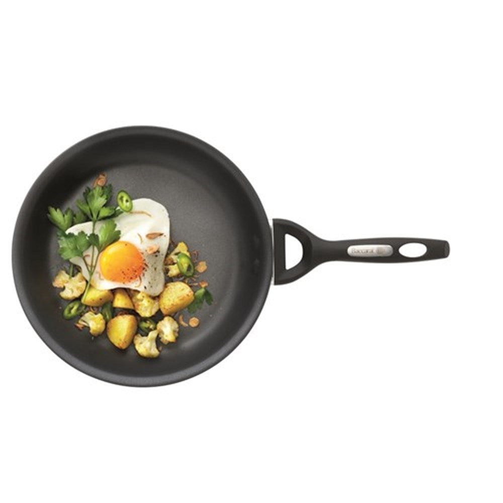 A black frying pan with vegetables including green peppers and tomatoes on a grey surface - Baccarat