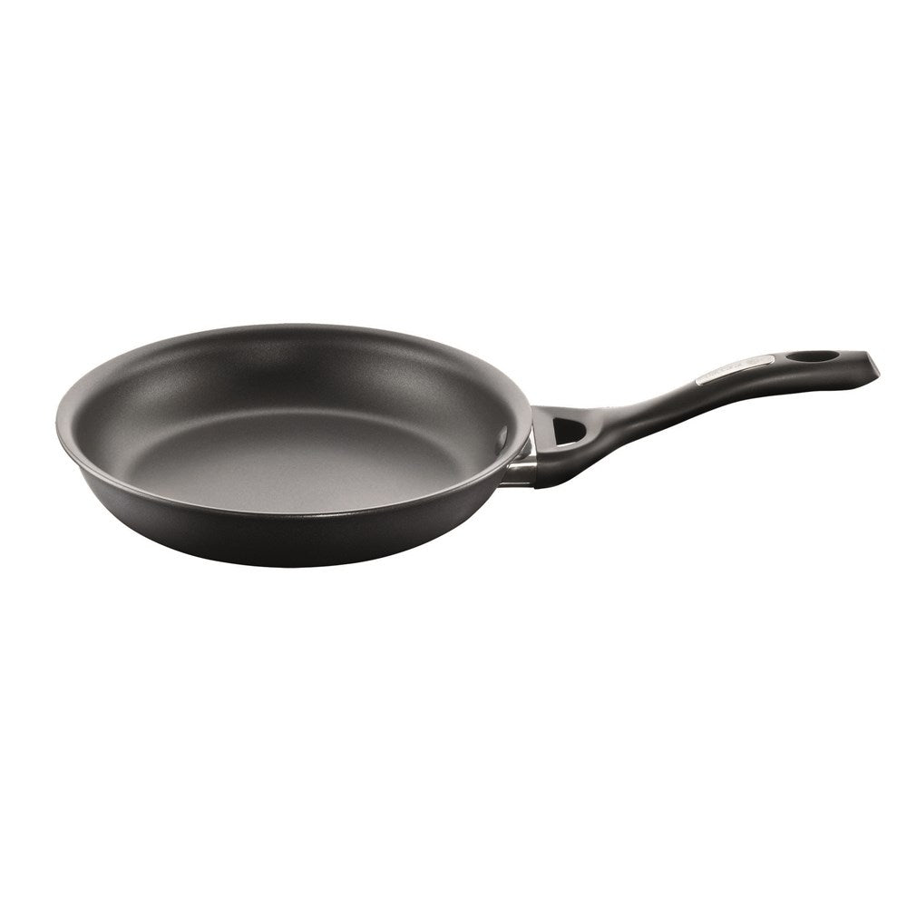 A black frying pan with vegetables including green peppers and tomatoes on a grey surface - Baccarat