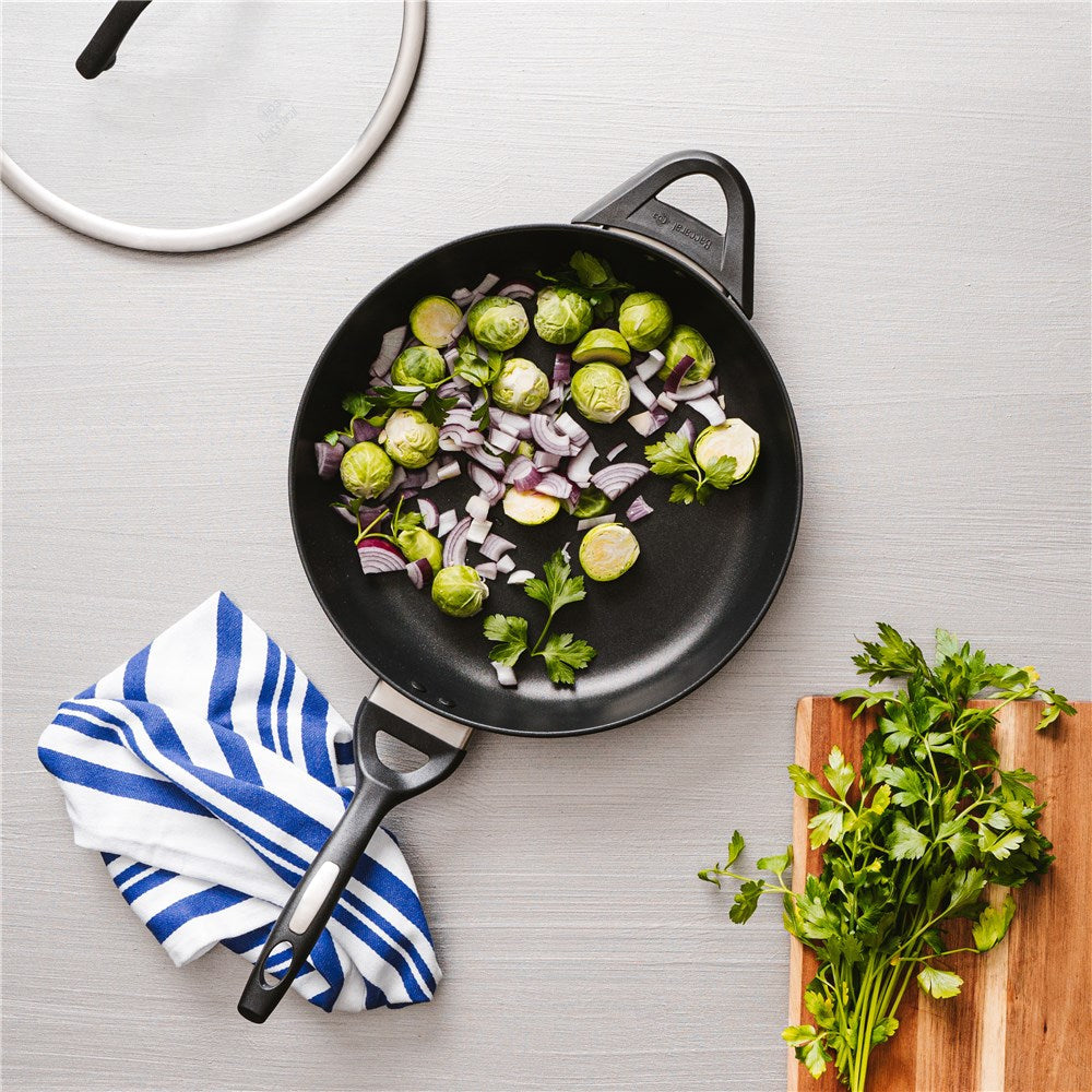 A sauté pan with chopped onions and green vegetables on a striped cloth - Baccarat