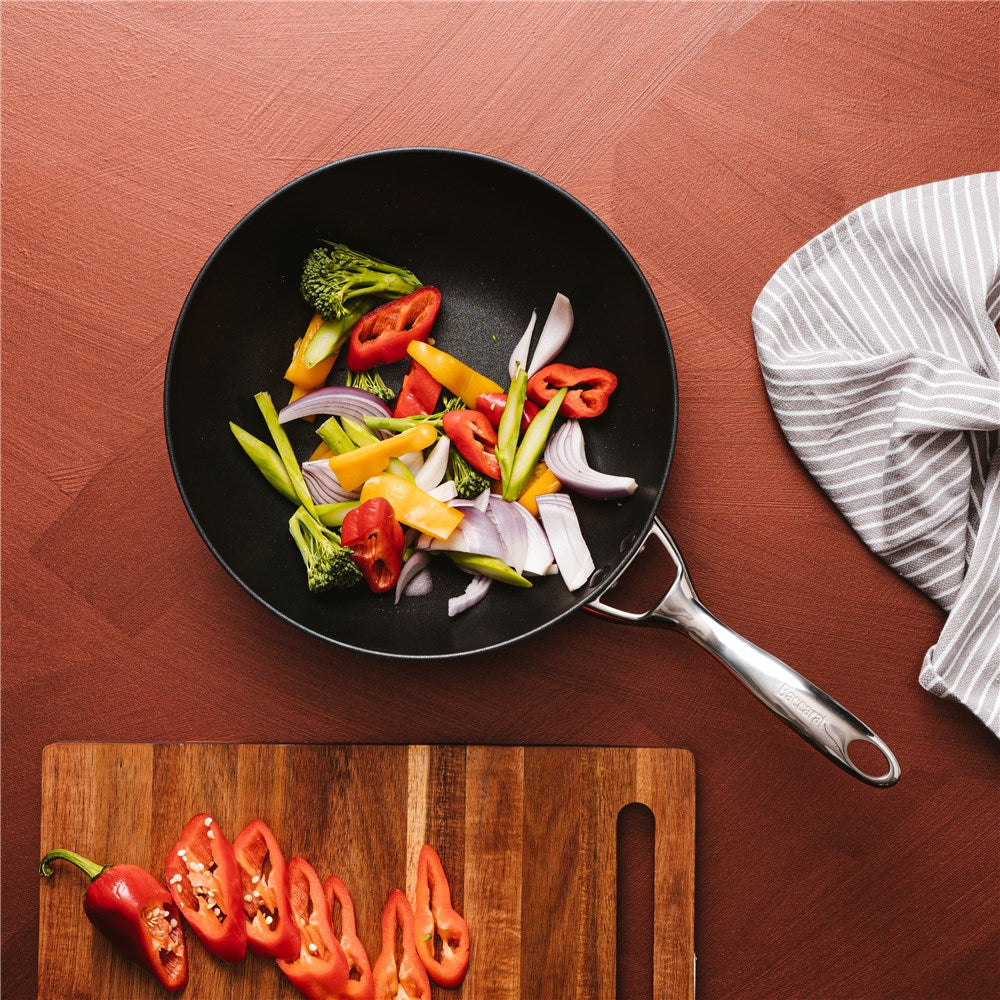 A stir fry pan filled with diced vegetables on a wooden board next to a grey cloth - Baccarat