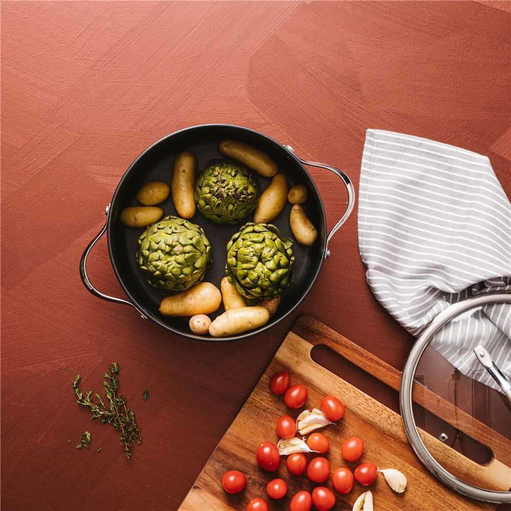 Top view of a black casserole with artichokes and potatoes on a table - Baccarat id3 Hard Anodised