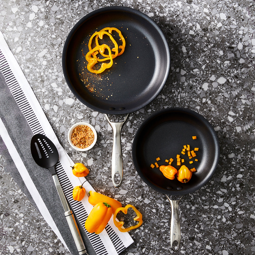 Two frying pans with bell pepper slices on a gray surface - Baccarat id3 hard anodised frypan