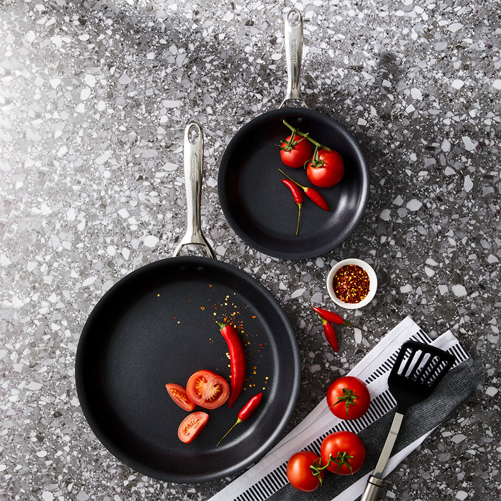Two hard anodised non stick frying pans with vibrant tomatoes and peppers - Baccarat