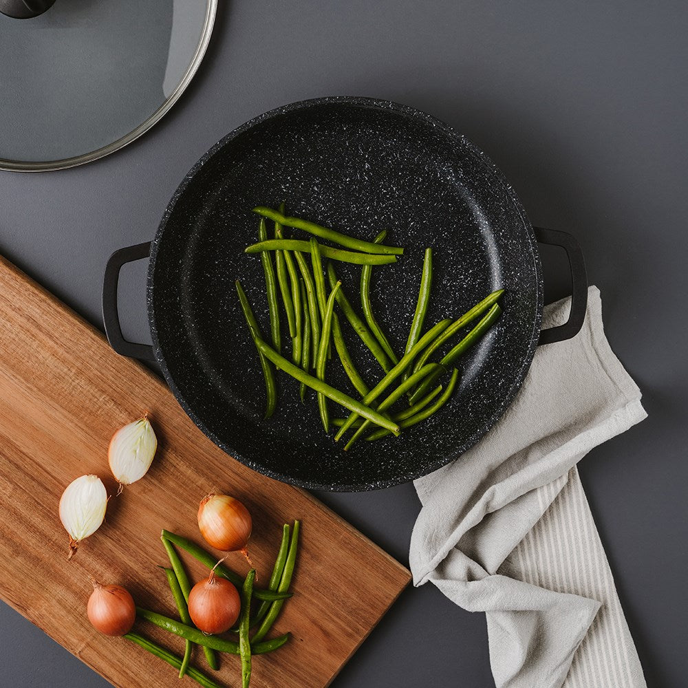 Overhead view of a frying pan filled with green beans and onions on a grey surface - Baccarat
