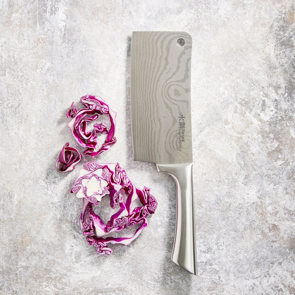 A Baccarat Damashiro cleaver with a sleek finish on a rustic surface surrounded by fresh ingredients