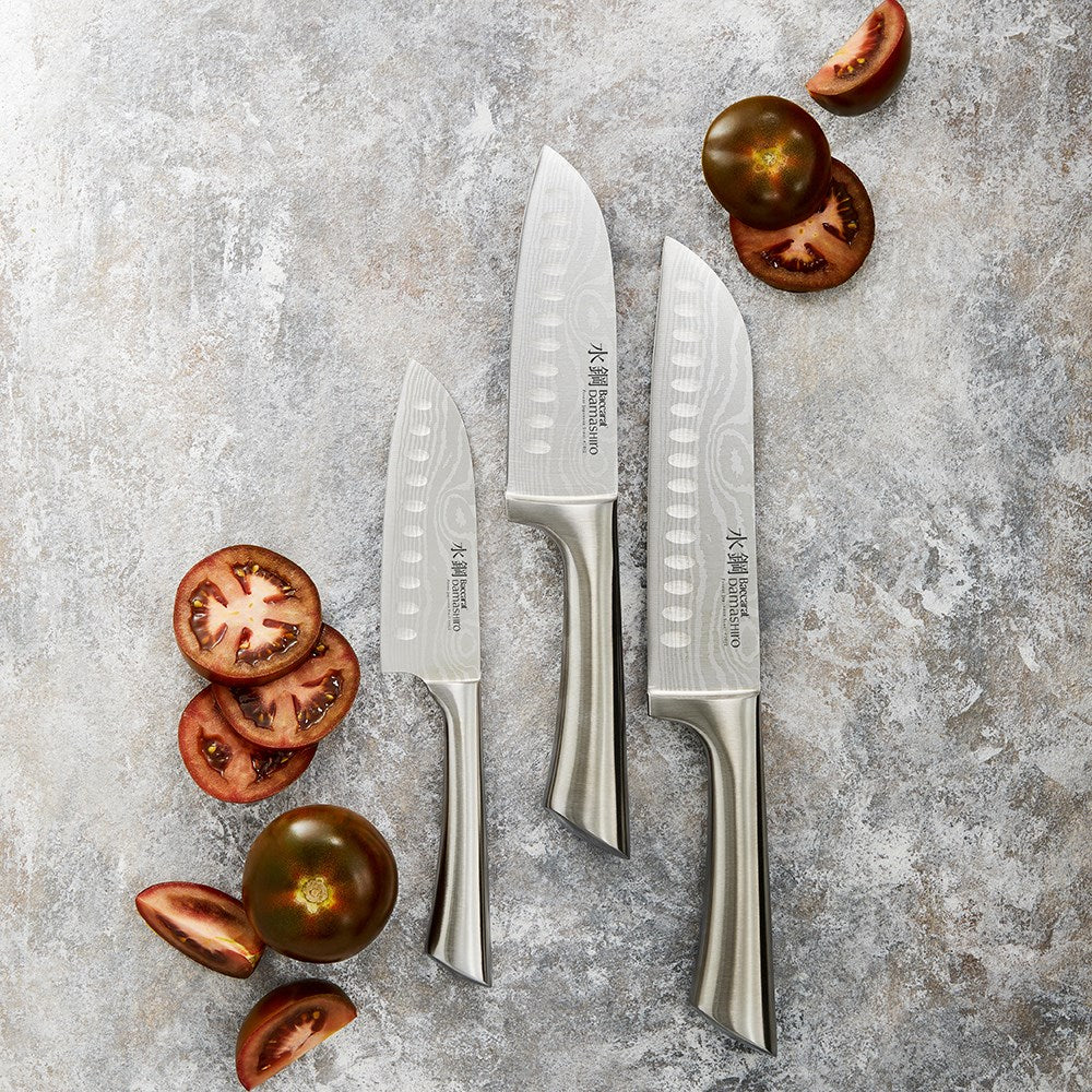 Three sleek santoku knives with textured blades on a gold and black background - Baccarat Damashiro
