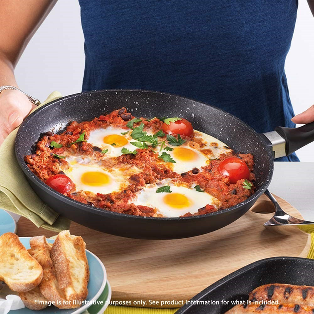 A hand holding a frying pan of shakshuka with sunny-side-up eggs in rich tomato sauce - Baccarat