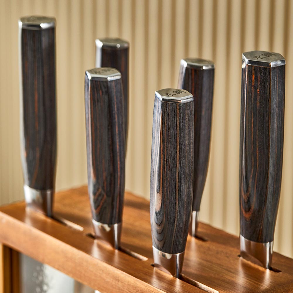 Seven sleek knives in a stylish wooden block on a countertop gleaming in light - Baccarat damashiro