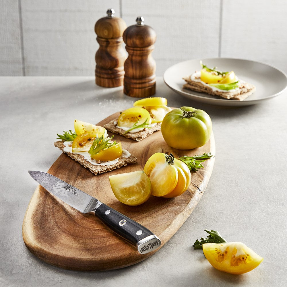 A wooden board with green tomatoes and crackers alongside a knife and pepper grinder set - Baccarat